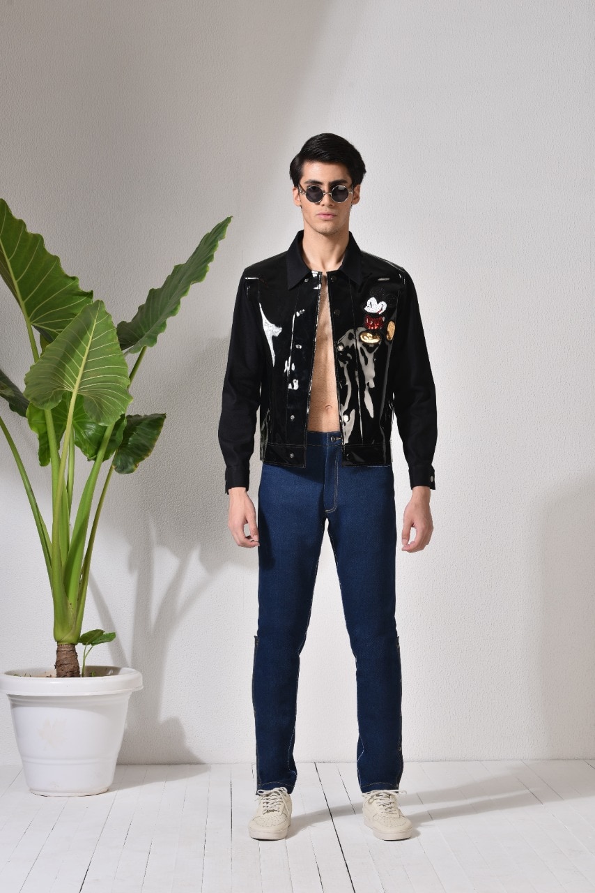 Abhishek Tibrewal’s statement jacket is made of thick synthetic sheet with sleeves in black denim to provide an ease of movement. The texture of black jacket is reflective and features an embroidered Mickey Mouse patch on one side