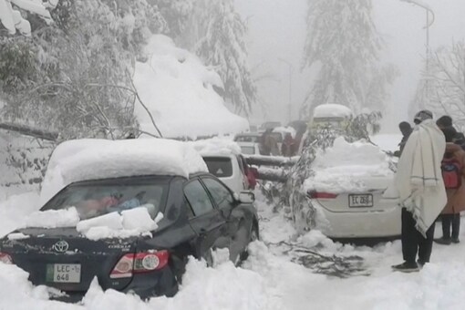 People stand next to cars stuck under fallen trees on a snowy road, in Murree, northeast of Islamabad. PTV/REUTERS TV via REUTERS 