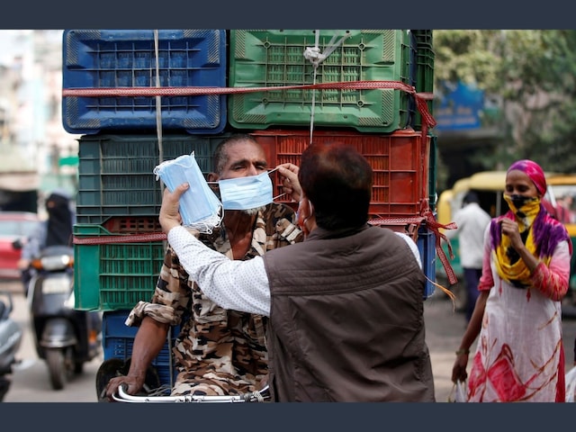 A social activist helps a rickshaw puller to wear a protective face mask as he distributes masks for free amidst the spread of the coronavirus disease (COVID-19) in India, January 6, 2022. REUTERS/Amit Dave