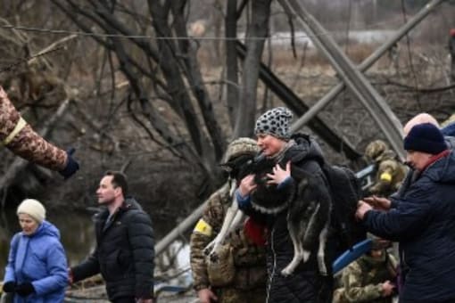 A woman carries a dog while people cross a destroyed bridge as they evacuate the city of Irpin in northwest of Kyiv, during heavy shelling and bombing on March 5. (Image: AFP)