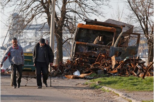 Local residents walk past a destroyed vehicle during Ukraine-Russia conflict in the southern port city of Mariupol, Ukraine, on April 20.  (Image Reuters) 
