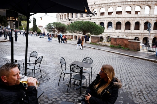 A man drinks a beer at a bar near the Colosseum as Italy begins to ease Covid restrictions in Rome, Italy (Image and Caption: REUTERS/Guglielmo Mangiapane)