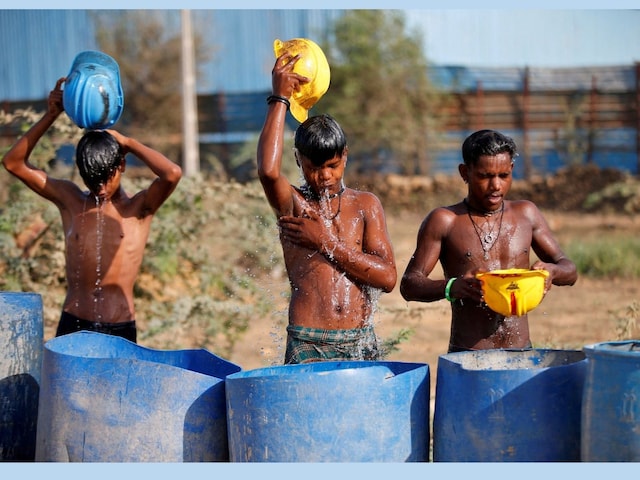 Workers use their helmets to pour water to cool themselves off near a construction site on a hot summer day on the outskirts of Ahmedabad, India, April 30, 2022. REUTERS/Amit Dave