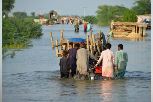 Men walk along a flooded road with their belongings in Sohbatpur, Pakistan, August 28, 2022. (Reuters)