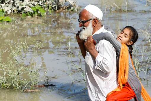 A man wades through flood waters carrying his grand daughter on his back following rains and floods during the monsoon season in Charsadda, Pakistan (Image: Reuters)
