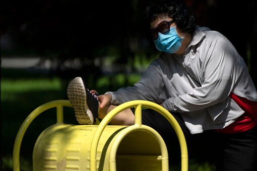 A woman wearing a face mask stretches on exercise equipment at a public park in Beijing, on Wednesday. (Image: AP Photo/Mark Schiefelbein)