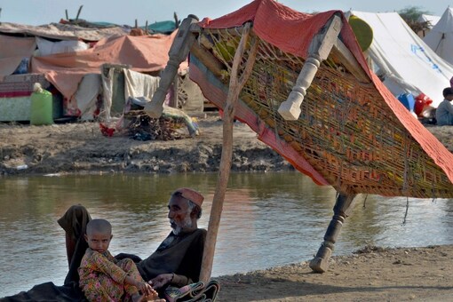 Flood victims sit under the shadow of a cot while they refuge on a roadside, in, Jaffarabad, a district of southwestern Baluchistan province, Pakistan, Monday, Sept. 19, 2022. (Image: AP) 