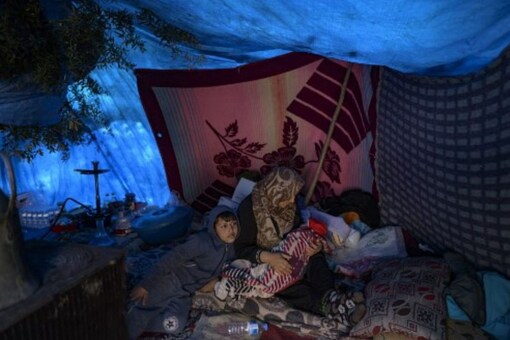 A Syrian woman sits in a tent near on the wreckage of a road destroyed in Demirkopru, a small Turkish village now divided by a large crack following two back-to-back massive earthquakes in Hatay on February 18, 2023. (Photo by Yasin AKGUL / AFP)