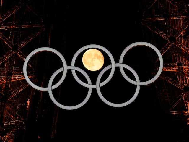 A full moon rises behind the Olympic rings hanging from the Eiffel Tower in Paris (AP)