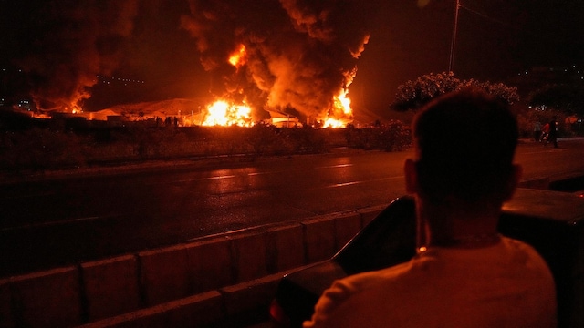 A man looks at flames rising from an oil storage facility after it appeared to have been struck by an Israeli strike in Tehran. (AP photo)