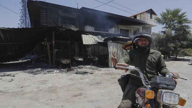 Syrian govt soldiers drive in front of a house that was burned during the clashes between the Syrian government forces and Druze militias on the outskirts of Sweida city. (AP Photo)