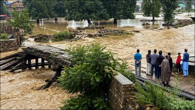 People stand near a partially damaged bridge as the Jhelum river flows in spate due to heavy rainfall. (PTI)