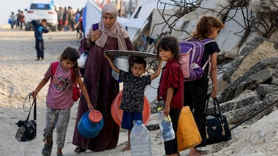 A displaced Palestinian woman, who fled Al-Shati (Beach) refugee camp in Gaza City with her children amid an Israeli military operation, following Israeli evacuation order, moves southward, in the central Gaza Strip. (IMAGE: REUTERS)