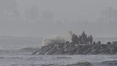 Cyclone Shakti: A police officer tries to move people away as high tide waves hit the Arabian Sea coast at Juhu Koliwada in Mumbai. (IMAGE: AP PHOTO)