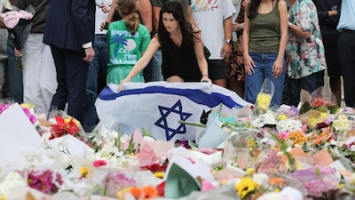 A mourner lays Israel's flag among floral tributes outside Bondi Pavilion in Sydney to honour victims of the Bondi Beach shooting. (AFP)