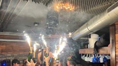 A photo going viral on social media appears to show people holding sparklers inside the Le Constellation bar in Crans-Montana shortly before the deadly New Year fire. The image has been widely shared online amid claims about what may have triggered the blaze. News18 could not independently verify the authenticity of the photo. (IMAGE: X/@visegrad24)  - Algorithmically enhanced image