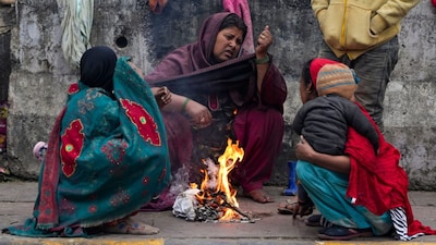 Women warm themselves near a small fire amid cold winter weather on a roadside, in New Delhi. (File/PTI)