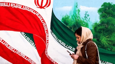 An Iranian woman walks past a mural of an Iranian flag in Tehran on February 22, 2026. (AFP Photo)
