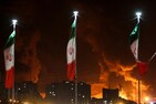 Iranian flags fly as fire and smoke from an Israeli attack on Sharan Oil depot rise on June 15, 2025. (Image: Reuters)
