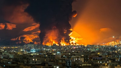 A tall plume of smoke billows from a fire next to Azadi Tower (C) following strikes near Mehrabad International Airport in Tehran. Image/X