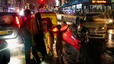 People cross a busy road amid rain using a cloth to shield themselves at Daryaganj, in New Delhi, Wednesday, March 18, 2026. (PTI)