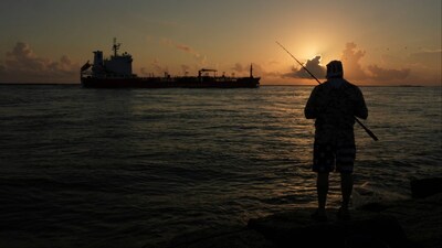 An oil tanker passes at sunrise while a man fishes in Port Aransas, Texas (Photo: AP)
