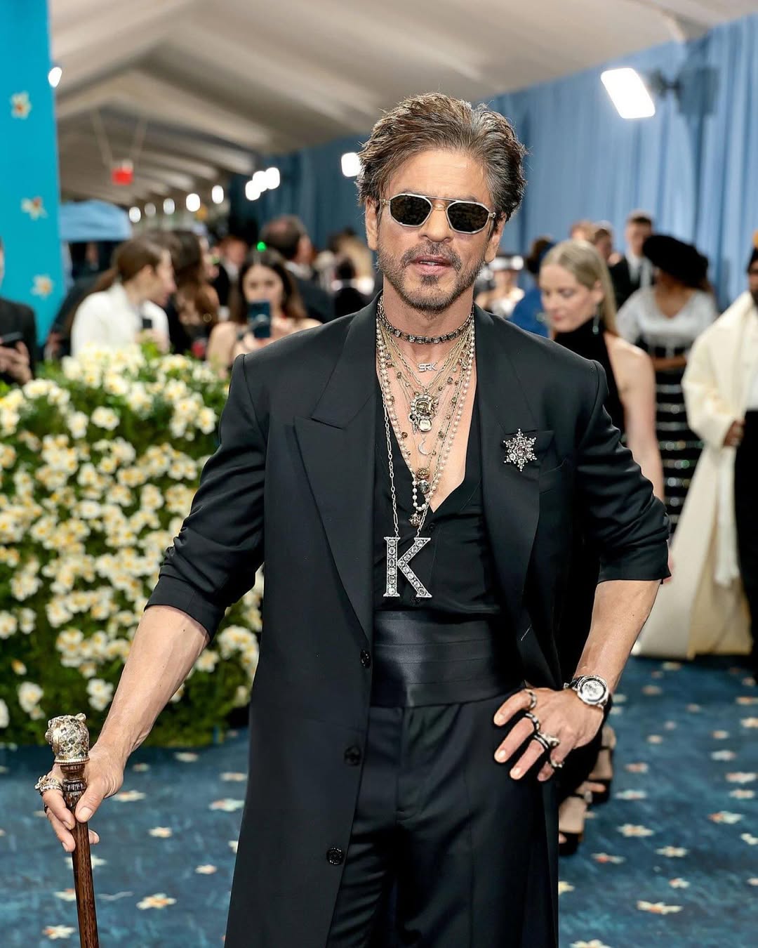 Shah Rukh Khan: Making his Met Gala debut, Shah Rukh Khan channelled dandyism in a sharp all-black Sabyasachi ensemble. A rhinestone-studded “K” pendant, layered jewellery, and a cane brought in a touch of drama, while his tousled hair, dark sunglasses, and leather boots added his unmistakable signature edge. (Image: Instagram)