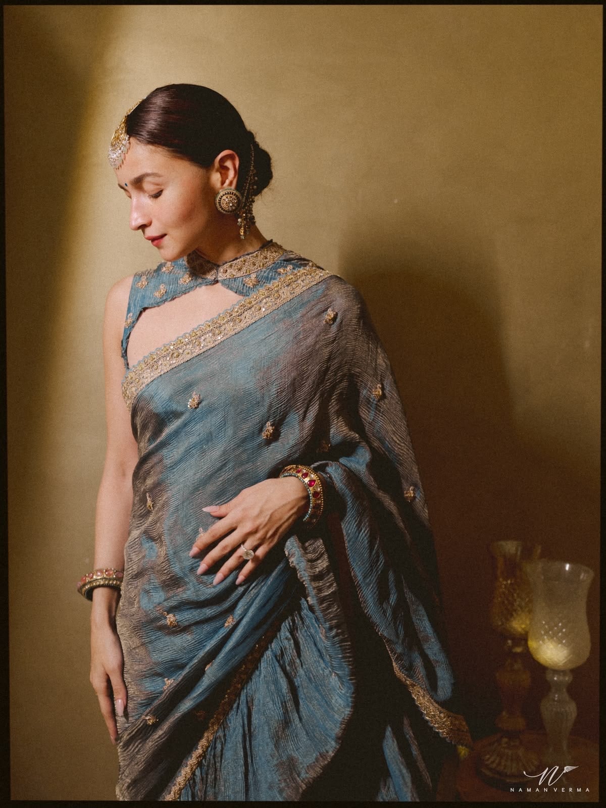 This look reimagines the classic saree blouse with a regal high-neck cape design. Intricate gold embroidery, a structured collar and elegant shoulder cut-outs add a contemporary twist while perfectly complementing the understated blue saree.