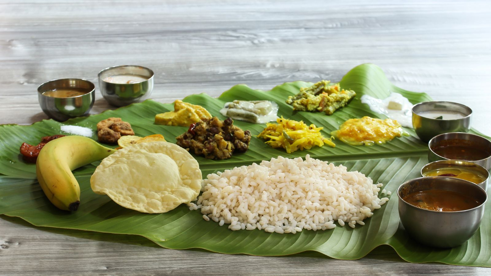 The Savoury SpreadA traditional Sadya can include a dazzling variety of dishes. Avial, a mix of vegetables cooked with coconut, is among the best-known preparations, while Olan combines ash gourd and beans with coconut milk. Thoran, Kalan, Erissery, Kootu Curry, Theeyal, Pachadi and Kichadi add different textures and flavours. Sambar, rasam, parippu and moru curry complete the progression, creating a balance between spicy, tangy, creamy and mildly flavoured dishes.