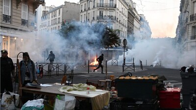A protester runs through tear gas while a flea market is taking place during clashes between protestors and police officers in Paris (Photo: AP)