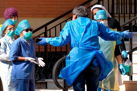 Medical personnel discussing outside the retirement home Giovanni XIII, where coronavirus swabs were carried out on the staff of the facility, after the death of a patient, in Rome, Tuesday, March 24, 2020. For most people, the new coronavirus causes only mild or moderate symptoms. For some it can cause more severe illness, especially in older adults and people with existing health problems. (Mauro Scrobogna/LaPresse via AP)