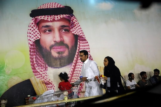 A Saudi family walk past a giant poster of Saudi Crown Prince Mohammed bin Salman, at a shopping mall in  Jiddah, Saudi Arabia, Sunday, Sept. 15, 2019. The weekend drone attack on one of the world's largest crude oil processing plants that dramatically cut into global oil supplies is the most visible sign yet of how Aramco's stability and security is directly linked to that of its owner -- the Saudi government and its ruling family. (AP Photo/Amr Nabil)