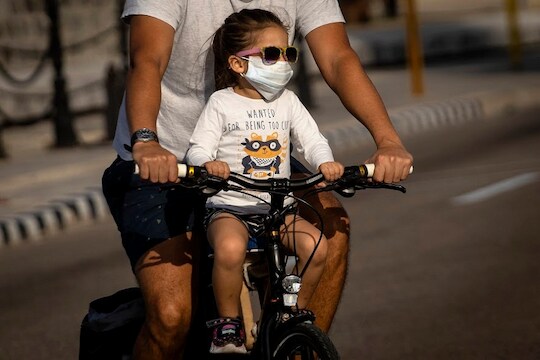 A girl wearing a protective face mask as a preventive measure against the spread of the new coronavirus ride a bicycle with her father in Havana, Cuba, Saturday, March 21, 2020. (AP Photo/Ramon Espinosa)