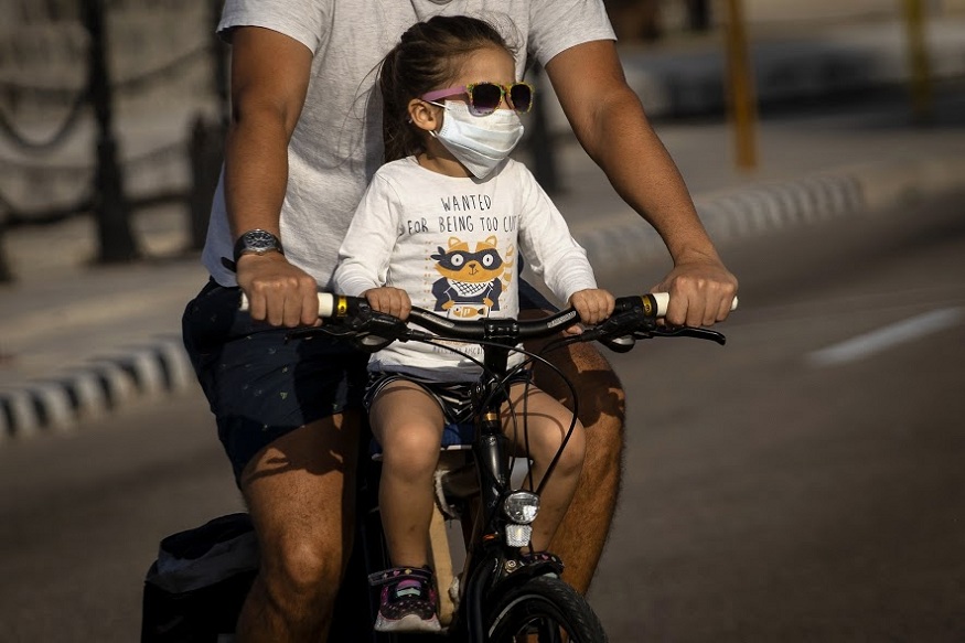 A girl wearing a protective face mask as a preventive measure against the spread of the new coronavirus ride a bicycle with her father in Havana, Cuba, Saturday, March 21, 2020. (AP Photo/Ramon Espinosa)