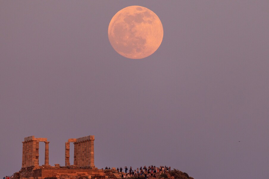  People watch a full moon, known as the Flower Moon, rising behind the Temple of Poseidon, before a lunar eclipse in Cape Sounion, near Athens, Greece, on Sunday. (Image: Reuters)