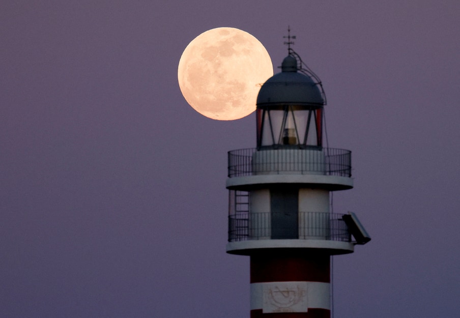 Full moon known as the Flower Moon rises behind the Arinaga lighthouse, before a lunar eclipse on the island of Gran Canaria, Spain, on Sunday. (Image: Reuters)