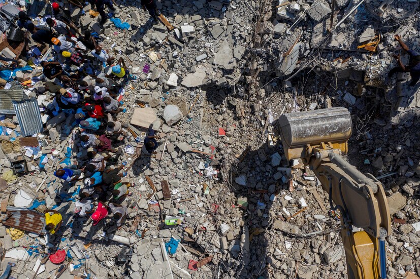 People watch an excavator removing rubble from the site of a collapsed hotel after 7.2 magnitude quake, in Les Cayes, Haiti on August 16. (Image: REUTERS/Ricardo Arduengo)
