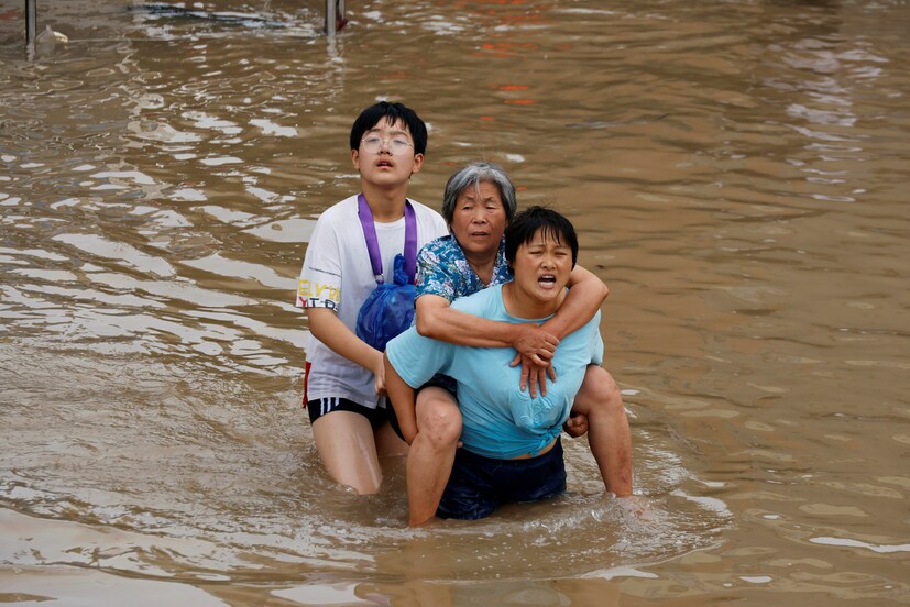 A woman carries an elderly woman as they make their way through floodwaters following heavy rainfall in Zhengzhou, Henan province, China on July 23. (Image: REUTERS/Aly Song)
