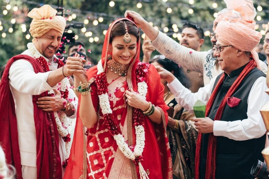 দেখা যাচ্ছে সোনালি জরির কাজ করা লাল বেনারসি শাড়ির সাজে নায়িকাকে, মাথায় বিয়ের সময়ে ছিল সোনালি কাজের লাল রেশমি ওড়না। সোনা আর মুক্তোর গয়নায়, খোঁপায় ফুলের সাজে একেবারে সাবেকি নববধূর রূপ ধরেছেন দিয়া। অন্য দিকে, বৈভব স্ত্রীর মতো বিশেষ সাজগোজের দিকে যাননি। তাঁর বিয়ের সাজ সম্পূর্ণ হয়েছে সাদা কুর্তা আর চুড়িদারে; মাথায় শোভা পেয়েছে সোনালি পাগড়ি। দেখা যাচ্ছে সোনালি জরির কাজ করা লাল বেনারসি শাড়ির সাজে নায়িকাকে, মাথায় বিয়ের সময়ে ছিল সোনালি কাজের লাল রেশমি ওড়না। সোনা আর মুক্তোর গয়নায়, খোঁপায় ফুলের সাজে একেবারে সাবেকি নববধূর রূপ ধরেছেন দিয়া। অন্য দিকে, বৈভব স্ত্রীর মতো বিশেষ সাজগোজের দিকে যাননি। তাঁর বিয়ের সাজ সম্পূর্ণ হয়েছে সাদা কুর্তা আর চুড়িদারে; মাথায় শোভা পেয়েছে সোনালি পাগড়ি।
