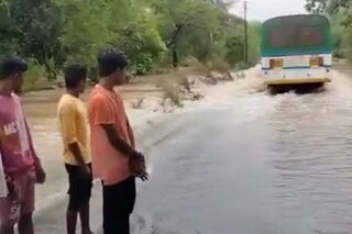 Locals watch as the driver tries to navigate the bus through a submerged bridge. (News18)