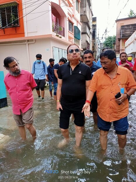 কামারহাটি পুরসভার ১১ নং ওয়ার্ড-এ এদিনও প্রায় হাঁটু সমান জল। সেই জলমগ্ন অবস্থা ঘুরে দেখলেন মদন মিত্র (Madan Mitra)। কালো টাইট টি-শার্ট, কালো প্যান্টের সঙ্গে চোখে ছিল কালো রোদচশমাটিও। জলে নেমে পাড়ায় পাড়ায় জল ঠেঙিয়ে পায়ে হেঁটে ঘোরেন বিধায়ক মদন মিত্র (TMC MLA)। ঘরে ঘরে গিয়ে মানুষের খোঁজ নেন, কথা বলেন কামারহাটির বিধায়ক। মানুষের সুবিধে অসুবিধে, জল নামানোর উপায় ইত্যাদি নিয়ে পুর-প্রশাসনের কর্তাদের পরামর্শ দেন মদন (Madan Mitra)।