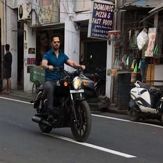 ভিড় রাস্তায় হঠাৎ বুলেট বাইকের আওয়াজ! বাইকের আওয়াজের উৎসের দিকে ঘাড় ঘোরাতেই হাঁ রাস্তার সাধারণ মানুষ! কাকে দেখছেন তাঁরা? ভরা বাজারে বাইক চালাচ্ছেন বলিউড অভিনেতা বরুণ ধাওয়ান! বৃহস্পতিবার, বরুণ ধাওয়ানকে হঠাৎই কানপুরের রাস্তায় নীল শার্ট পরে বুলেট চালাতে দেখে এভাবেই অবাক হয়ে যান শহরের বাসিন্দারা। প্রথমে কেউই বিশ্বাস করেননি। পরে সিনেমার সেট ও শ্যুটিং দেখে ভিড় জমতে থাকে। বরুণ ধাওয়ান তাঁর আগামী সিনেমার শ্যুটিং করতে কানপুরে গিয়েছিলেন। সেখানেই নির্দিষ্ট লোকেশনে শ্যুটিং টিম সেট তৈরি করেছিল। কিন্তু শ্যুটিংয়ের শিডিউল এত তাড়াতাড়ি ঠিক হয়েছিল যে কারও কাছেই আগে থেকে কোনও তথ্য ছিল না।