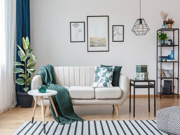 Black table next to sofa with green blanket in cozy apartment interior with gallery of posters