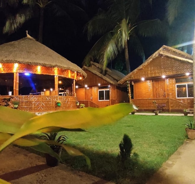 সবটাই প্রকৃতির সঙ্গে মিশে থাকা সাদামাটা, শান্ত আর পরিবেশ বান্ধব এক আবহ। কিন্তু ভেতরে ঢুকলেই যেন অন্য এক জগত। কাঠে খোদাই করা সূক্ষ্ম কারুকার্য, আলোর নরম ছোঁয়া, নিপুণ সাজসজ্জা—সব মিলিয়ে কটেজের ভিতরটা হয়ে ওঠে ছবির মতো মনোরম। (Photo -Facebook)