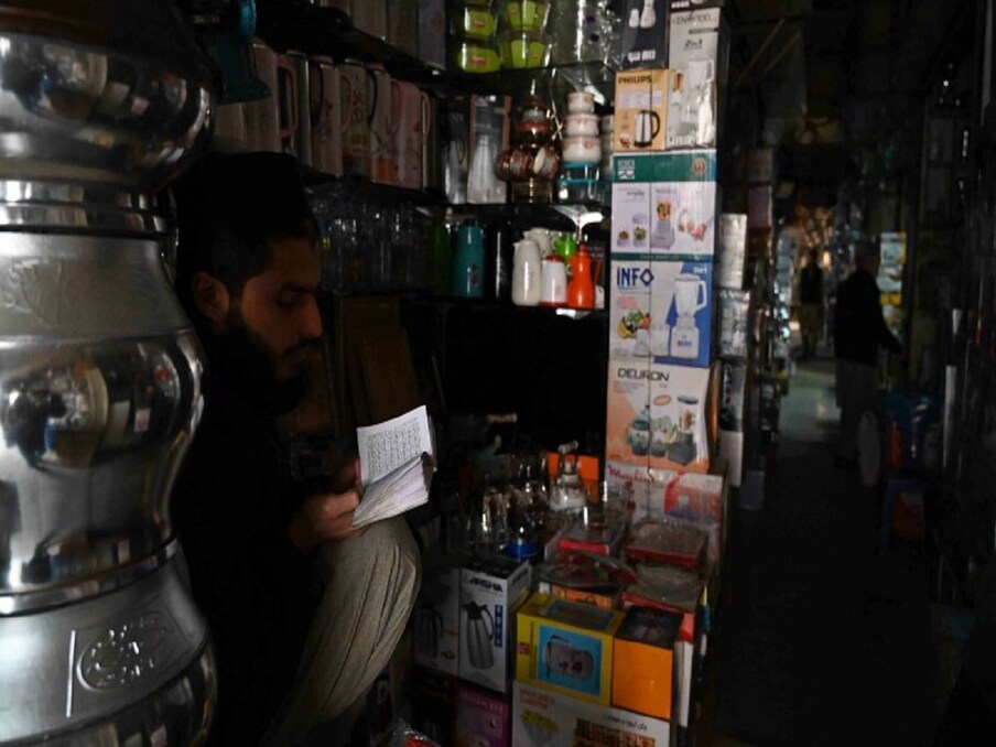  ایک دکاندار اپنی دکان میں بجلی کٹوتی کے بعد قرآن پاک پڑھ رہا ہے۔ لوگ اپنی دکانوں پر موجود تو ہیں لیکن بجلی نہ ہونے کی وجہ سے خریدار سامان کو ٹھیک سے نہیں دیکھ پا رہے ہیں جس کی وجہ سے دکانداروں کو شدید پریشانی کا سامنا کرنا پڑا ہے۔ (تصویر: اے ایف پی)