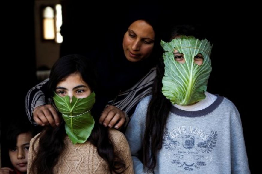 A Palestinian mother entertains her children with makeshift masks made of cabbage in Gaza Strip. (Image: AP) A Palestinian mother entertains her children with makeshift masks made of cabbage in Gaza Strip. (Image: AP)